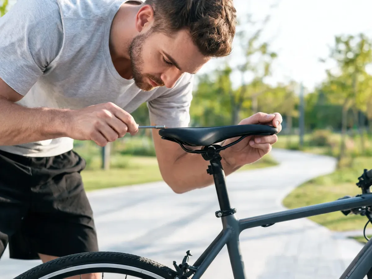 Mężczyzna na ścieżce rowerowej reguluje wysokość siodełka miejskiego roweru kluczem imbusowym.