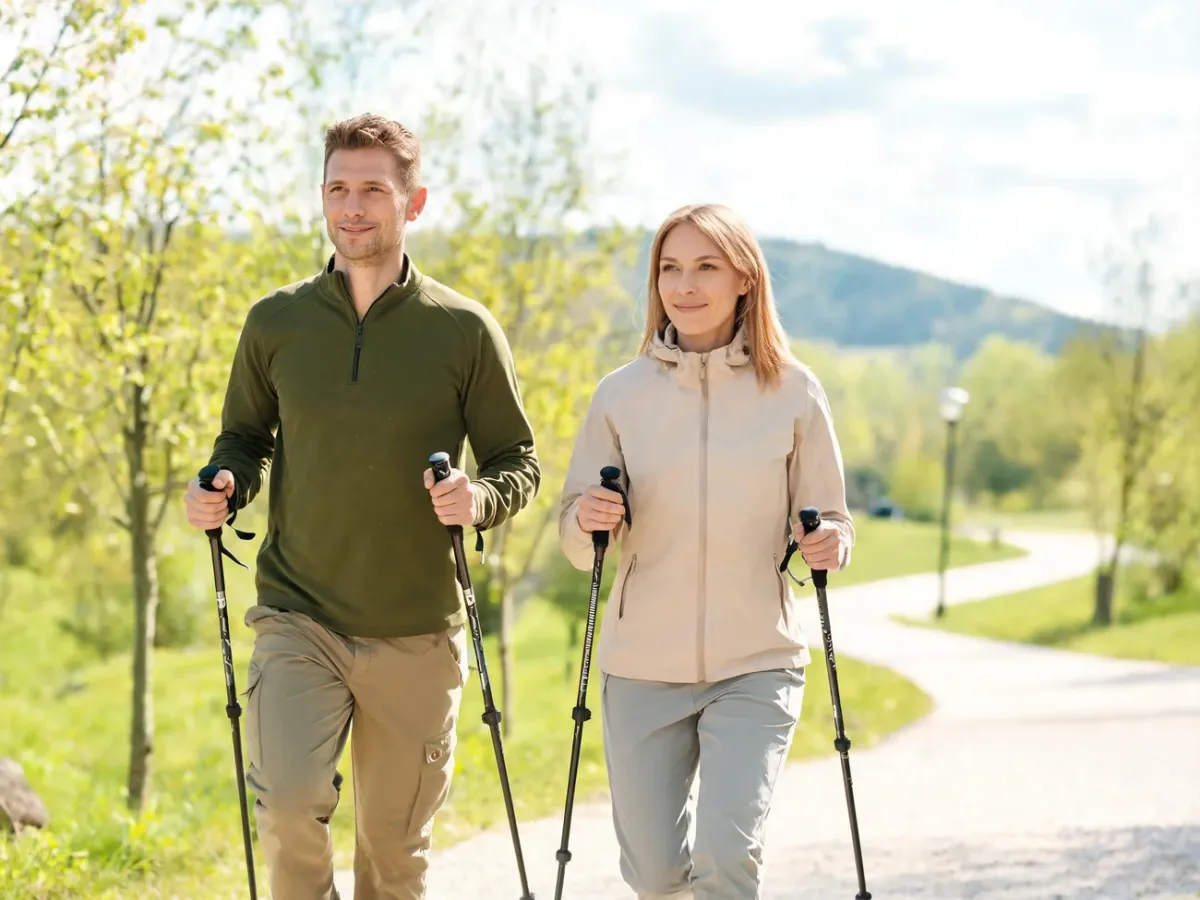 Para dorosłych uprawiająca nordic walking w słonecznym parku, dynamiczny marsz z kijkami w zielonym, wiosennym otoczeniu.