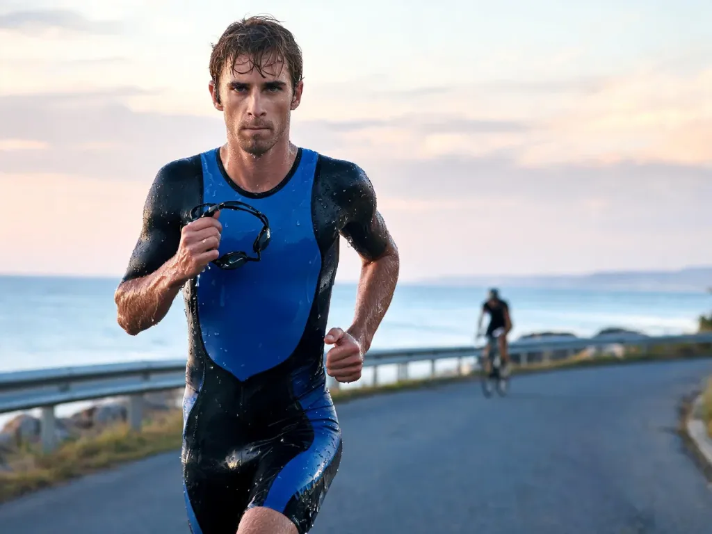Triathlonista na trasie Ironmana biegnie wzdłuż wybrzeża o świcie, zmęczony po pływaniu, ale skoncentrowany na celu
