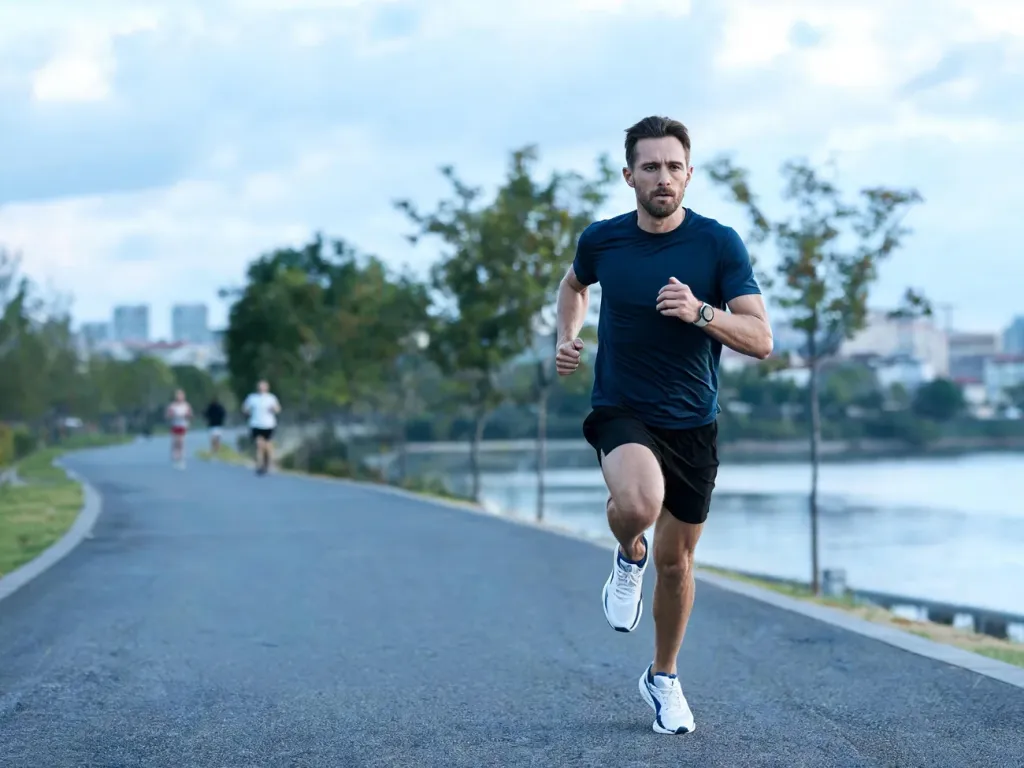 Biegacz w średnim tempie na nadmiejskiej ścieżce o świcie, ilustrujący trening do półmaratonu w miejskim otoczeniu.